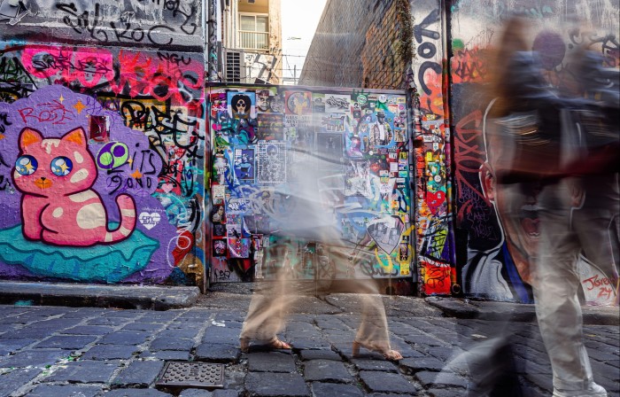 Murals and graffiti on the walls of Hosier Lane in Melbourne, with blurred images of people passing by
